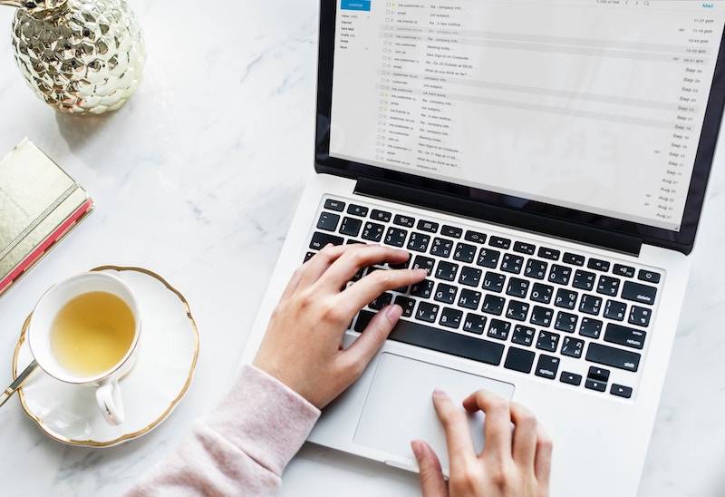 A woman with her laptop open, checking emails and drinking tea.
