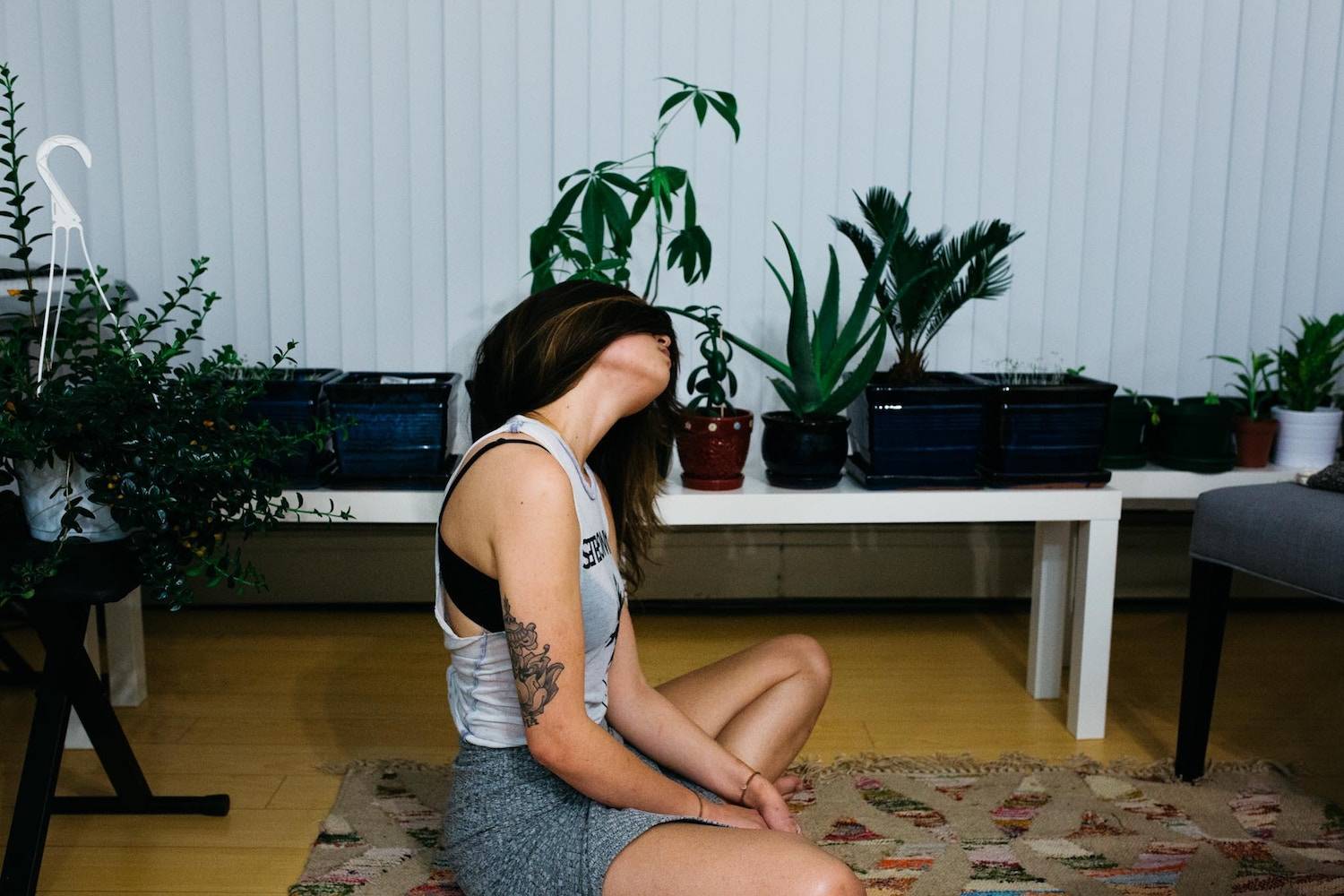 A brunette woman stretches in her living room, which is full of plants.